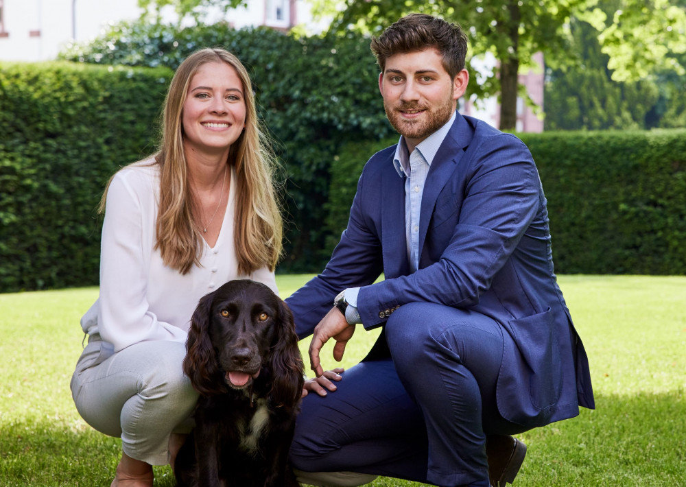 Ein Mann und eine Frau hocken auf einer Wiese der Eventlocation bei Wiesbaden mit einem braunen Hund